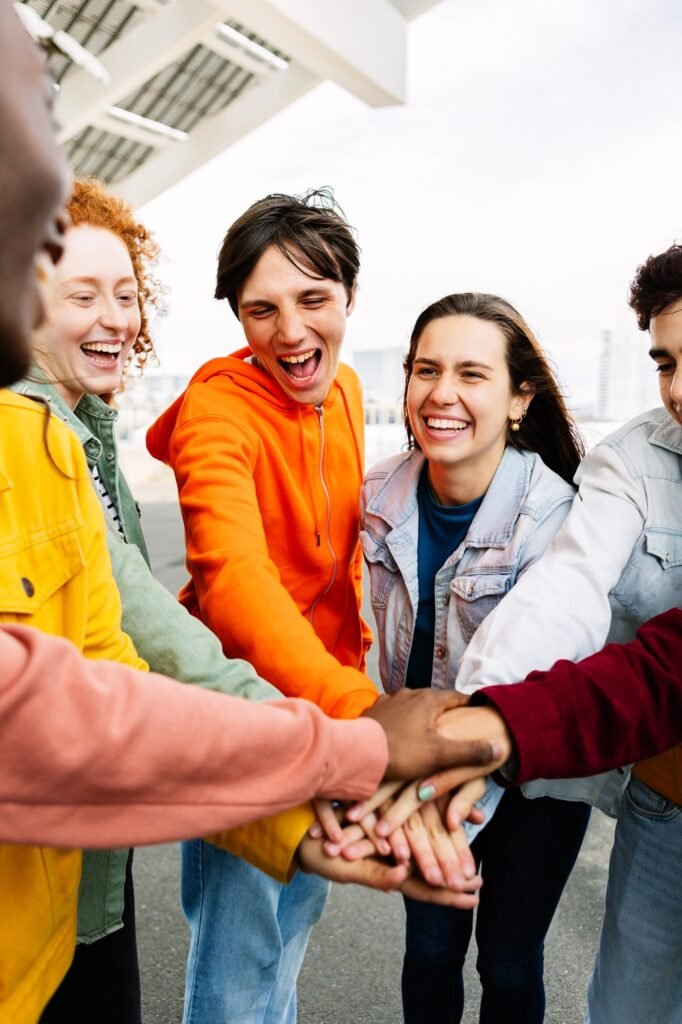 Young happy people stacking hands together outside.